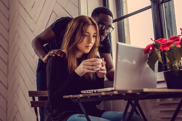 Hombre afroamericano y mujer caucásica usando laptop en la mesa.