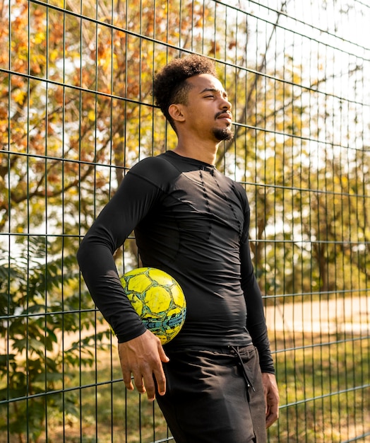 Hombre afroamericano posando con una pelota de fútbol en un campo