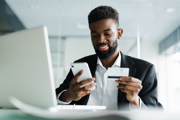 Hombre afroamericano que paga con tarjeta de crédito en línea mientras realiza pedidos a través de Internet móvil haciendo transacciones utilizando la aplicación de banco móvil.