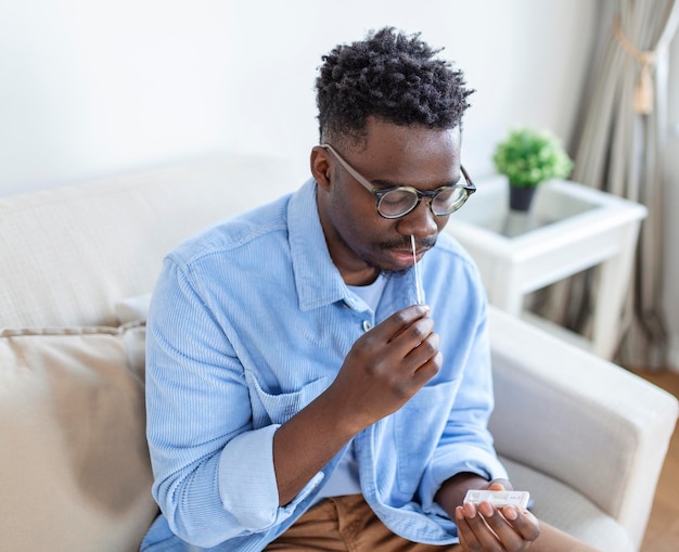 Foto gratuita hombre afroamericano que usa un hisopo de algodón mientras realiza una prueba pcr de coronavirus en casa hombre que usa una prueba de diagnóstico rápido de coronavirus hombre joven en casa que usa un hisopo nasal para covid19