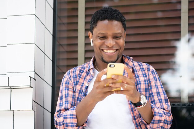 Hombre afroamericano que usa su teléfono móvil mientras está sentado en el escaparate de una tienda en la calle. Concepto urbano.