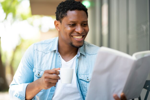 Hombre afroamericano relajarse y leer un libro mientras está sentado en una cafetería.