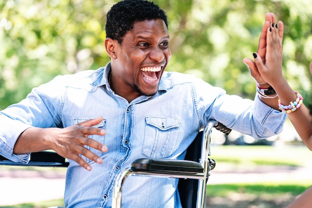 Hombre afroamericano en silla de ruedas disfrutando y divirtiéndose con su hija en el parque.