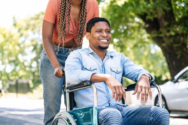 Un hombre afroamericano en silla de ruedas disfrutando de un paseo al aire libre con su novia