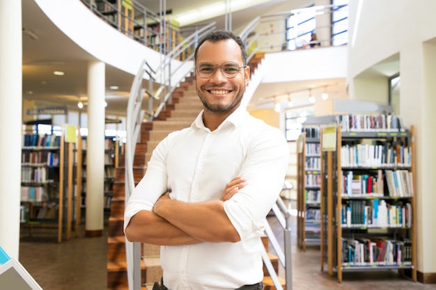 Hombre afroamericano sonriente que presenta en la biblioteca pública