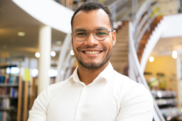 Hombre afroamericano sonriente que presenta en la biblioteca