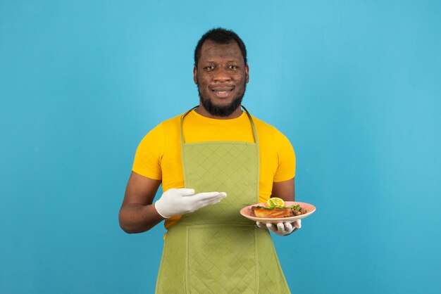 Hombre afroamericano sosteniendo un plato de comida en la mano, se encuentra sobre la pared azul.