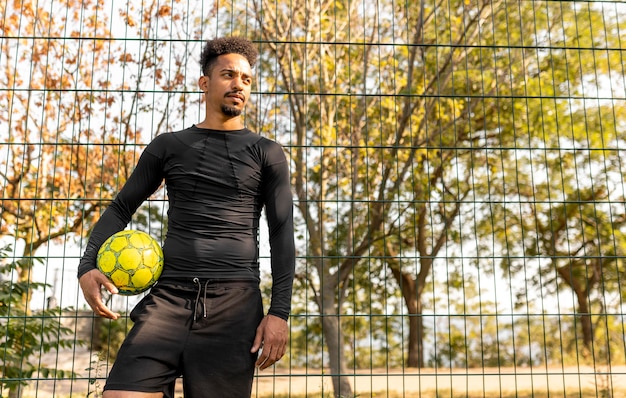 Hombre afroamericano de tiro largo posando con un balón de fútbol con espacio de copia