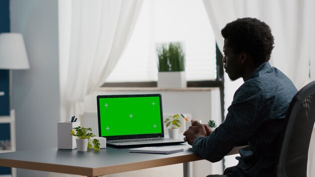 Hombre afroamericano usando laptop maqueta con pantalla verde