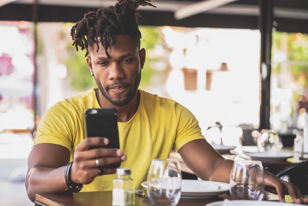 Hombre afroamericano usando su teléfono móvil mientras está sentado en un restaurante.