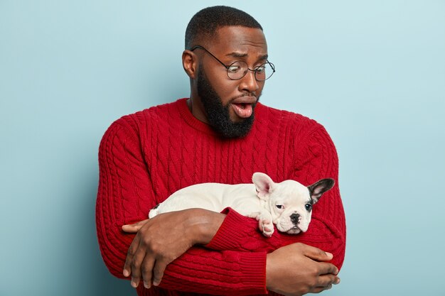 Hombre afroamericano vestido con suéter rojo y sosteniendo perrito