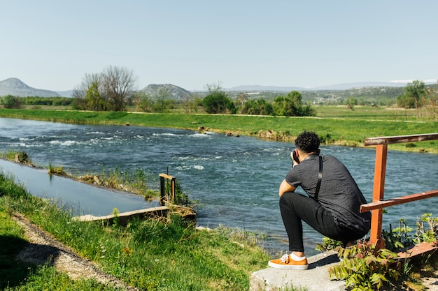 Hombre agachado tomando foto de río idílico