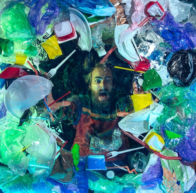 Hombre ahogado en agua debajo de la pila de recipientes de plástico, basura. Ecología, concepto de medio ambiente