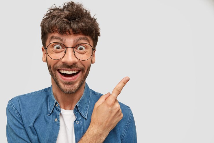Foto gratuito hombre alegre con amplia sonrisa, tiene expresión divertida, indica a un lado, anuncia algo increíble