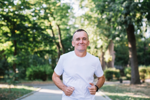 Hombre alegre en camiseta blanca corriendo en un parque