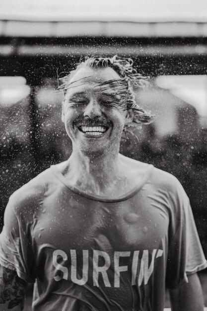 Un hombre alegre con una camiseta brillante con una patineta en un parque de patinaje se ríe, el agua le salpica el pelo.