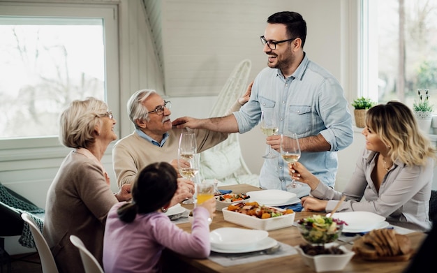 Hombre alegre divirtiéndose mientras propone un brindis a su familia durante el almuerzo