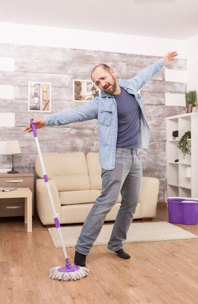 Hombre alegre divirtiéndose trapeando el piso del apartamento