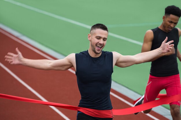 Hombre alegre joven atleta cruzando la línea de meta