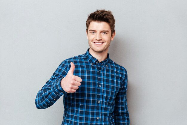 Hombre alegre joven estudiante sosteniendo pulgar aislado