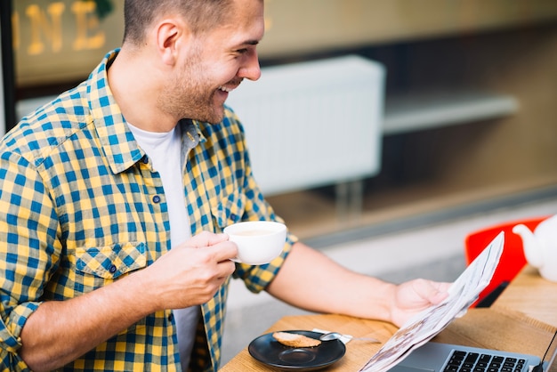 Hombre alegre leyendo periódico y tomando café