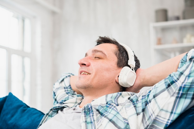 Hombre alegre con los ojos cerrados escuchando música en los auriculares en el sofá