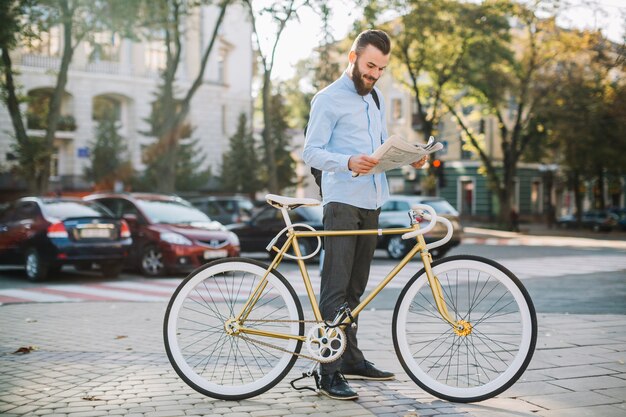 Hombre alegre que lee el periódico cerca de la bici