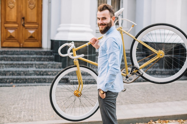 Hombre alegre que lleva la bicicleta en hombro