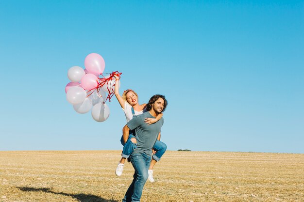 Hombre alegre que lleva a mujer con globos