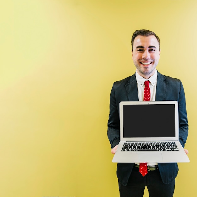 Hombre alegre que muestra la computadora portátil en la cámara