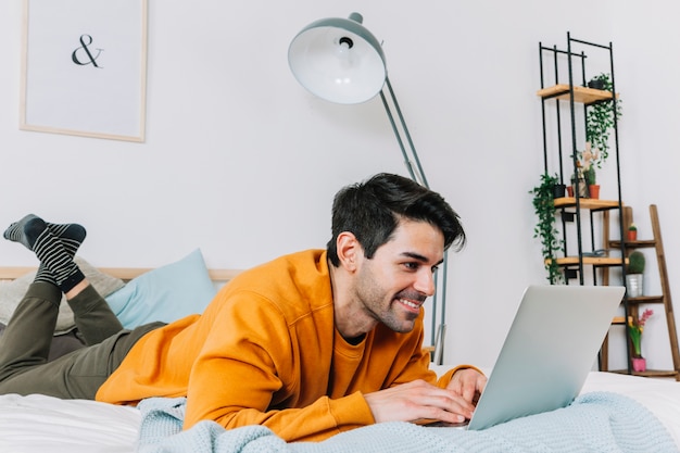 Hombre alegre que usa la computadora portátil en dormitorio con estilo