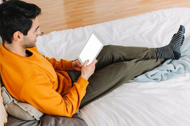 Hombre alegre que usa la tableta en cama cómoda