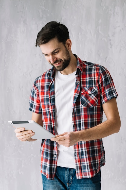 Hombre alegre que usa la tableta cerca de la pared