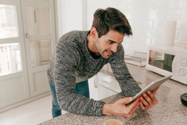 Hombre alegre que usa la tableta en cocina