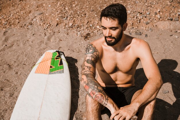 Hombre alegre sentado cerca de la tabla de surf