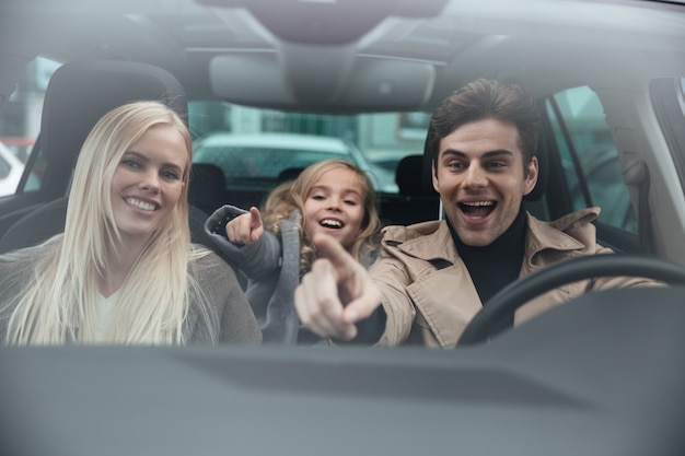 Hombre alegre sentado en coche con su esposa e hija