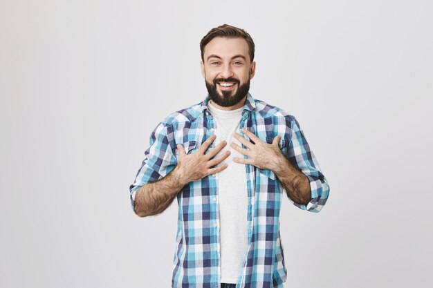 Hombre alegre sorprendido recibir regalo, tomarse de las manos en el pecho agradecido