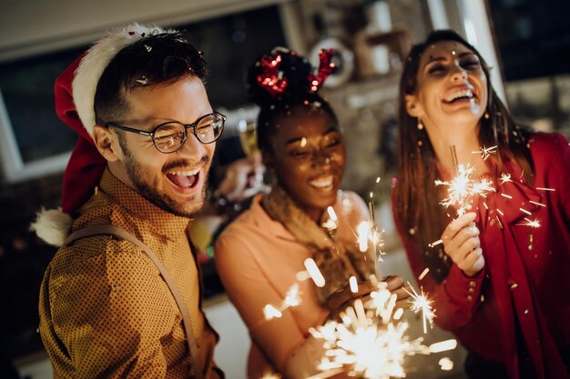 Hombre alegre y sus amigos divirtiéndose con bengalas en la víspera de Año Nuevo en casa