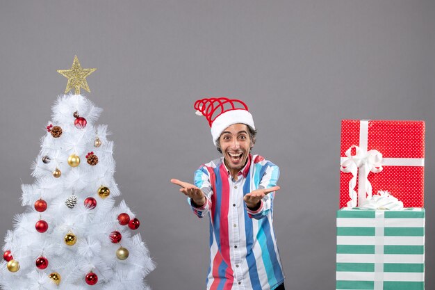 Hombre alegre vista frontal con las manos abiertas cerca del árbol de Navidad blanco