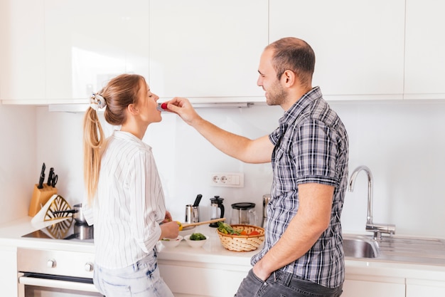 Hombre alimentando rábano rojo fresco y saludable a su novia en la cocina