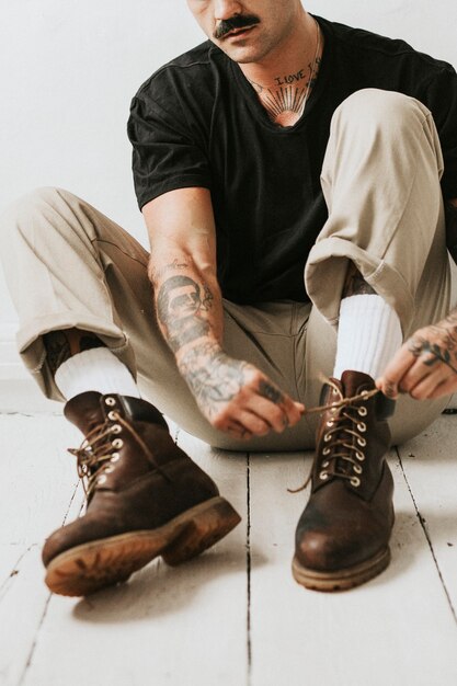Hombre alternativo atando los cordones de los zapatos de botas en el suelo