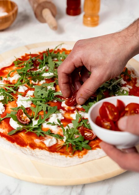 Hombre de alto ángulo poniendo tomates en pizza