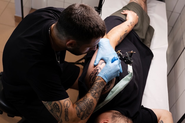 Hombre de alto ángulo tatuando con guantes