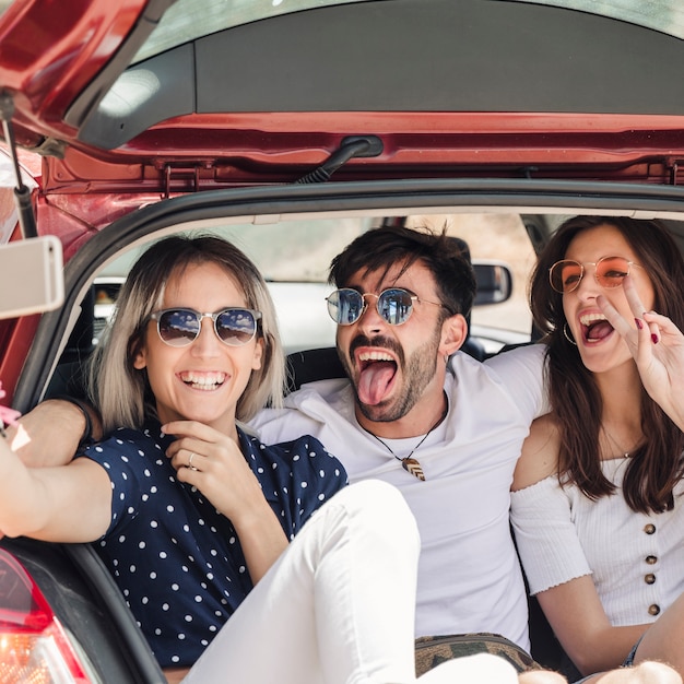 Hombre con amigas sentada en el carro del coche posando para autorretrato