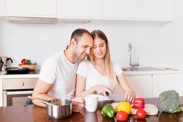 Hombre amoroso sentado con su esposa cortando las verduras con un cuchillo