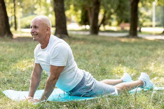 Hombre anciano feliz practicando yoga afuera