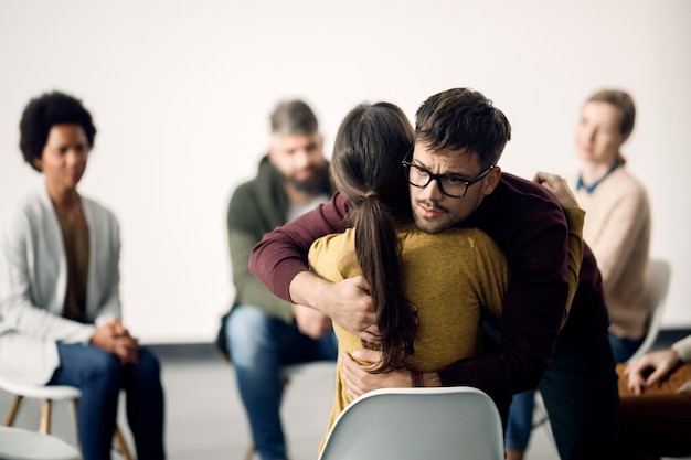 Hombre angustiado abrazando a uno de los asistentes a una terapia de grupo durante la reunión