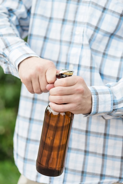 Hombre anónimo que abre cerveza en la naturaleza