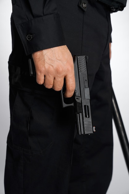 Foto gratuita un hombre anónimo con uniforme negro portando un arma de fuego de cañón corto bajó la vista de la cosecha