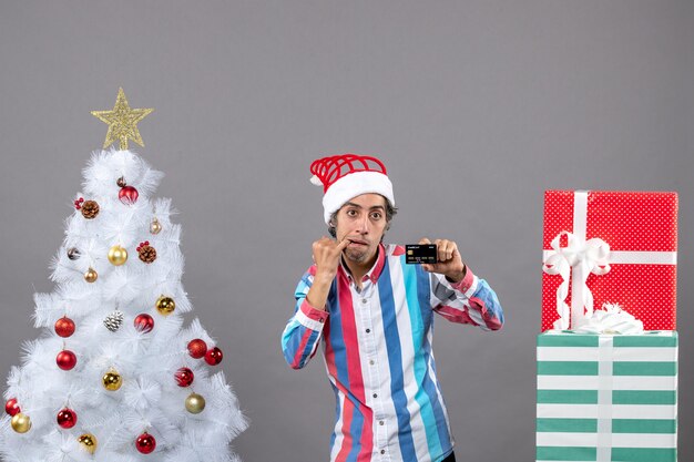 Hombre apático de vista frontal poniendo la mano en su ratón de pie cerca del árbol de Navidad blanco